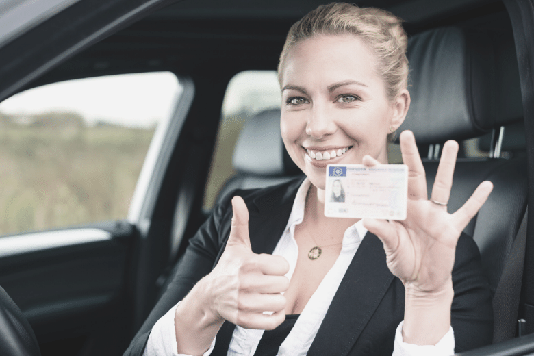 Fröhliche Frau zeigt ihren Führerschein und Daumen nach oben