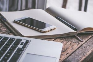 Auf einem Schreibtisch liegt ein Smartphone und ein Notizbuch.