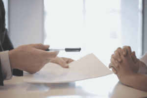 Zwei Hände sind zu sehen, die eine Hand hat einen Stift und Zettel in der Hand.