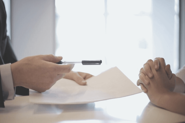 Zwei Hände sind zu sehen, die eine Hand hat einen Stift und Zettel in der Hand.